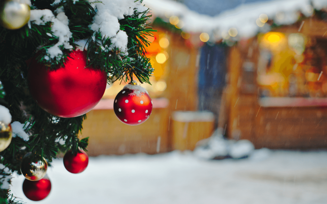 Ornements rouges et dorés sur un sapin enneigé avec des lumières floues en arrière-plan, créant une ambiance festive de Noël en extérieur.